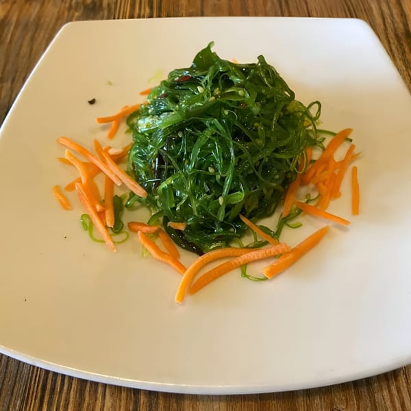 A vibrant green seaweed salad with shredded carrots on a white square plate at Sen Noodle House.