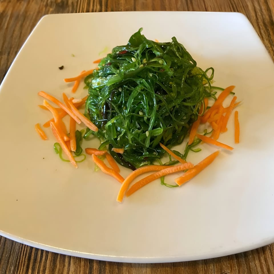 A vibrant green seaweed salad with shredded carrots on a white square plate at Sen Noodle House.