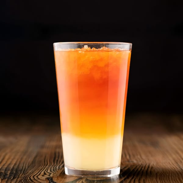 A vibrant, layered orange and yellow drink with ice, on a dark wooden table.
