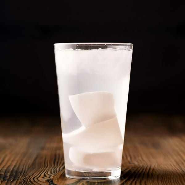 A clear glass of coconut water with large pieces of fresh coconut meat on a wooden table.